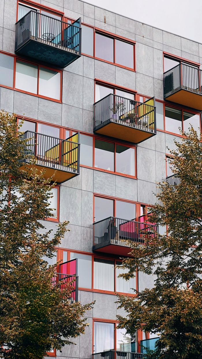 cta-02 Vertical view of a modern residential block with colorful balconies and trees.